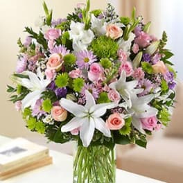 Mixed bouquet of white lilies, pink roses, and purple flowers in a glass vase