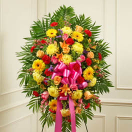 Standing floral spray with mixed bright flowers and a pink ribbon