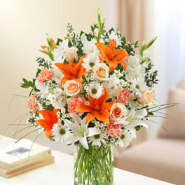 Bouquet of orange lilies, white daisies, and peach roses in a glass vase