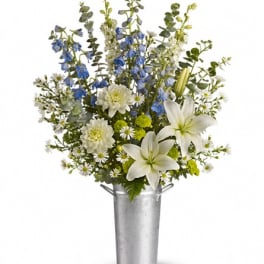 White lilies and blue flowers arranged in a tall metal vase