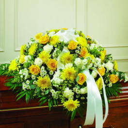 Yellow and white floral casket spray with ribbon on a wooden casket