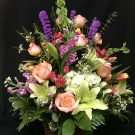 Mixed bouquet in a wicker basket with peach roses, lilies, and purple spikes