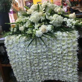 Large white floral arrangement with roses and lilies over a dense chrysanthemum base