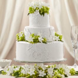 Three-tier white wedding cake with white and green floral accents