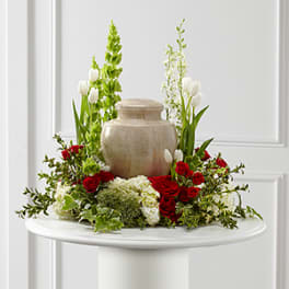 Red and white floral arrangement around a beige urn on a pedestal