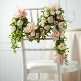Floral garland with pink orchids and white roses draped over a white chair