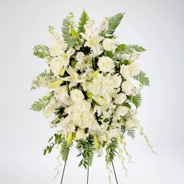 Tall white standing spray with roses, lilies, and ferns on a metal easel.