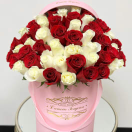 Red and white roses arranged in a pink hatbox on a small round table.
