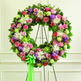 Floral wreath with pink, purple, white, and green blooms on a black stand