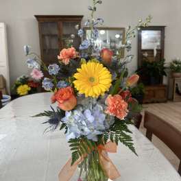 Mixed bouquet in a glass vase with yellow gerbera, blue hydrangea, and orange carnations