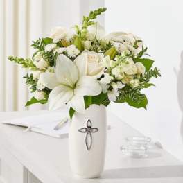 White floral arrangement in a tall vase with a cross emblem