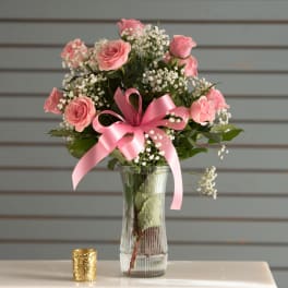 Tall glass vase with pink roses, white baby's breath, and a large pink bow