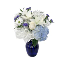 White lilies, daisies, and blue hydrangea in a cobalt vase with a white ribbon