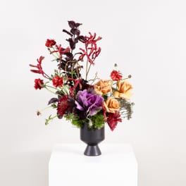 Tall floral arrangement in a black pedestal vase with red, purple, and peach blooms