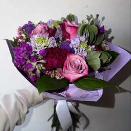 Handheld bouquet of pink and purple flowers wrapped in lavender paper