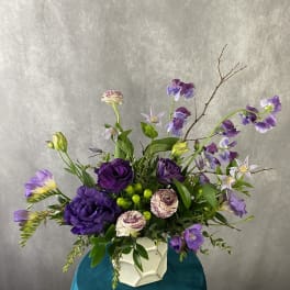 Purple and lavender floral arrangement in a white geometric vase