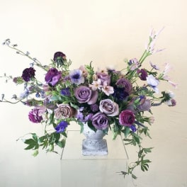 Lavender and purple floral arrangement in a white pedestal vase