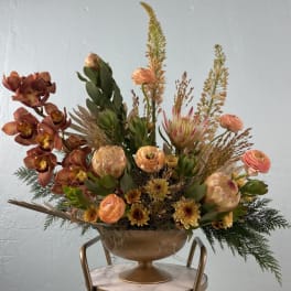 Rust-toned floral arrangement in a gold pedestal bowl