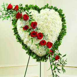 Heart-shaped white floral wreath with red roses on a stand