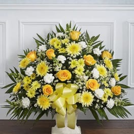Yellow roses and white daisies arranged in a standing spray with a ribbon bow