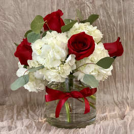 Red roses and white hydrangeas in a clear glass vase with a red ribbon