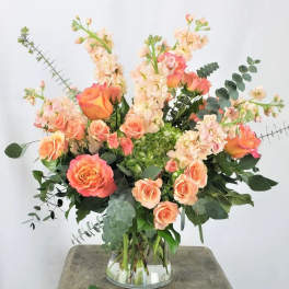 Peach and coral roses with pale pink stock in a clear glass vase
