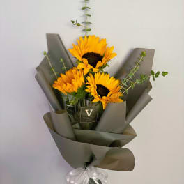 Bouquet of yellow sunflowers with tall eucalyptus stems wrapped in dark paper with a white ribbon bow