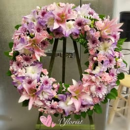 Pink and lavender wreath of lilies, carnations, and mums displayed on a wooden easel