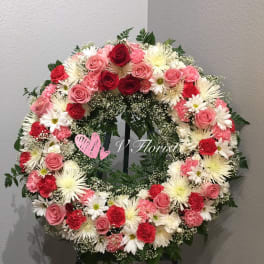 Standing wreath with pink and red roses, carnations, and white daisies on an easel