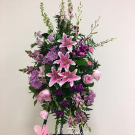 Tall floral standing spray with pink lilies and purple blooms on an easel