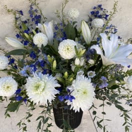 White lilies and blue flowers arranged in a black vase