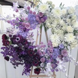 Large heart-shaped floral arrangement in purple, white, and burgundy tones on an easel