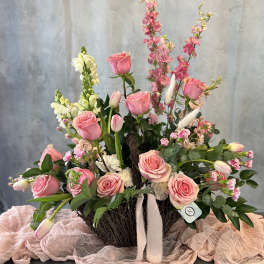 Pink roses and tulips arranged in a woven basket with white ribbon