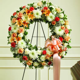 Floral wreath with orange roses, white mums, and a peach ribbon on a stand