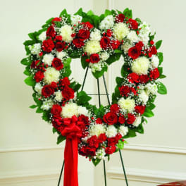 Heart-shaped wreath of red and white flowers on a stand with a red bow