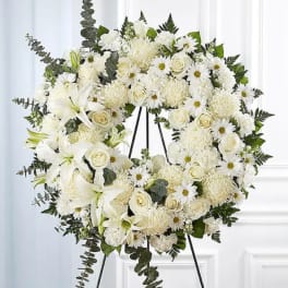 White floral wreath on a black easel with roses and lilies