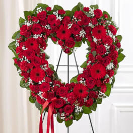 Heart-shaped red floral wreath on a stand with a red ribbon