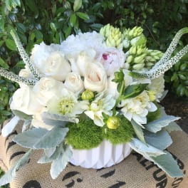 White roses and dahlias arranged in a white vase with green accents