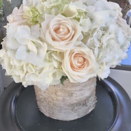 Cream roses and white hydrangeas arranged in a birch container