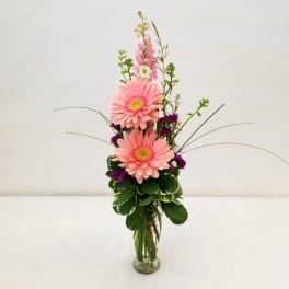Pink gerbera daisies in a clear glass vase with purple accents