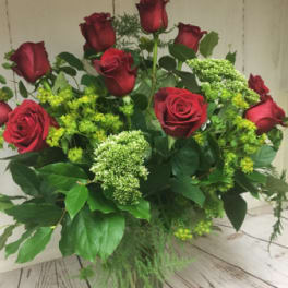 Tall arrangement of red roses with green filler flowers in a clear glass vase