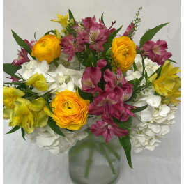 Mixed bouquet of white hydrangeas, yellow blooms, and pink alstroemeria in a clear glass vase