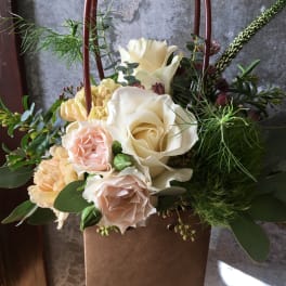 Cream and blush roses in a brown gift bag with greenery