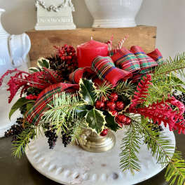 Holiday centerpiece with red candle, plaid ribbon, and evergreen sprigs