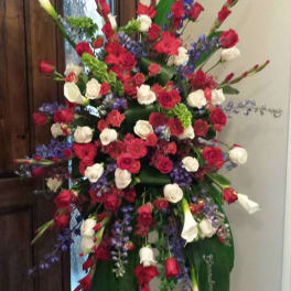 Tall standing spray of red and white roses with purple flowers and white calla lilies on a metal easel.
