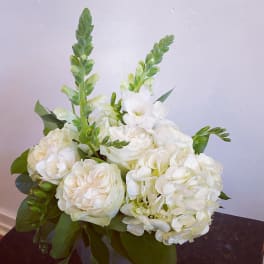 Compact white rose and hydrangea arrangement with snapdragon spikes in a glass vase