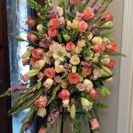 Tall standing spray of peach and cream roses with white lilies on a tripod easel.