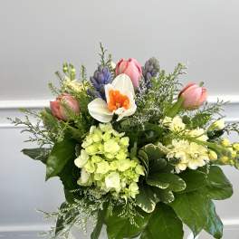 Spring bouquet with pink tulips, white daffodil, green hydrangea, and purple hyacinths in a white container