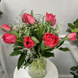 Vase of bright pink tulips with white filler flowers arranged in a textured glass vase