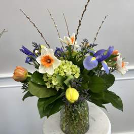 Springy mixed bouquet with daffodils, tulips, irises, and green hydrangea in a green glass vase
